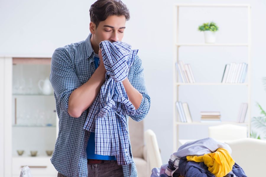 man smells clean pile of laundry as he folds it